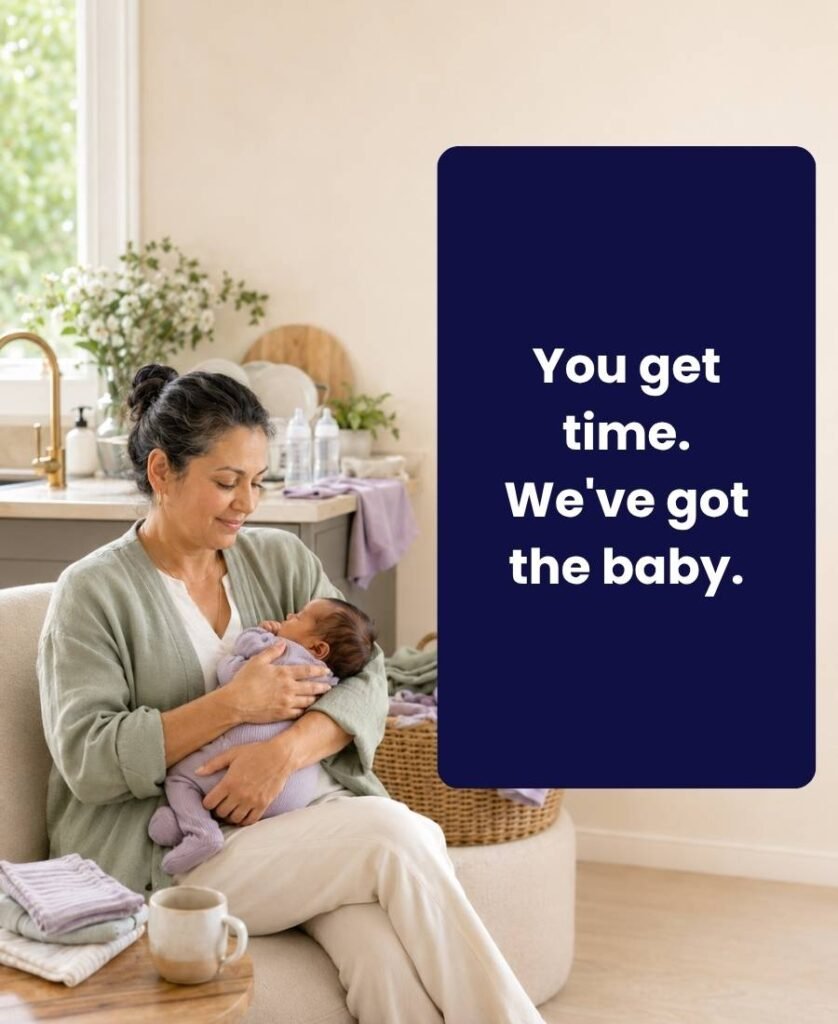 Daytime postpartum support worker holding a newborn while baby laundry and feeding supplies wait nearby in a bright home.